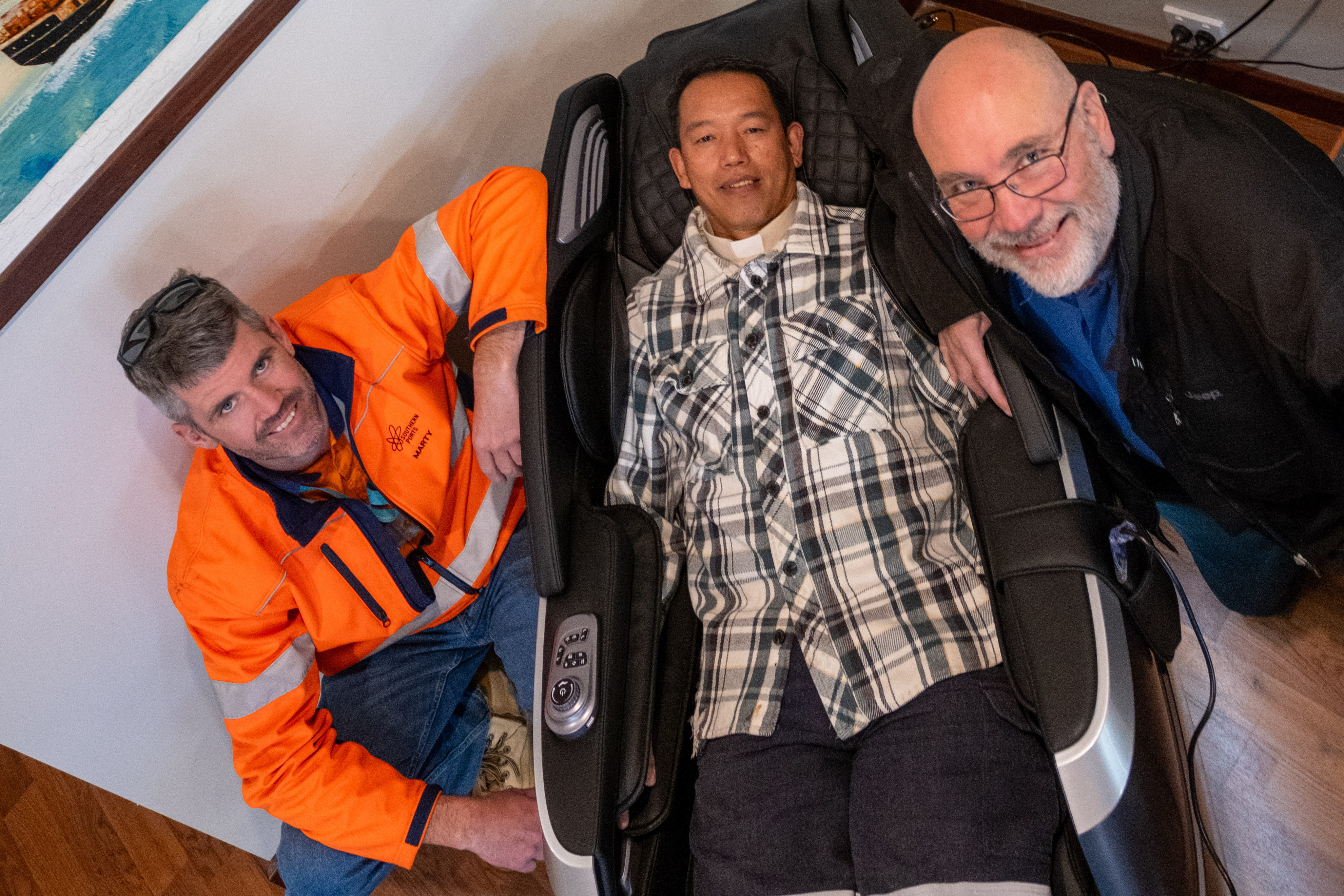 Southern Ports General Manager South West Marty Stafford and Bunbury Mission to Seafarers Centre Managers Very Rev. Darryl Cotton check out the new massage chair donated to Bunbury MTS as centre chaplain Reverend Gaerlan Baguil test the chair.